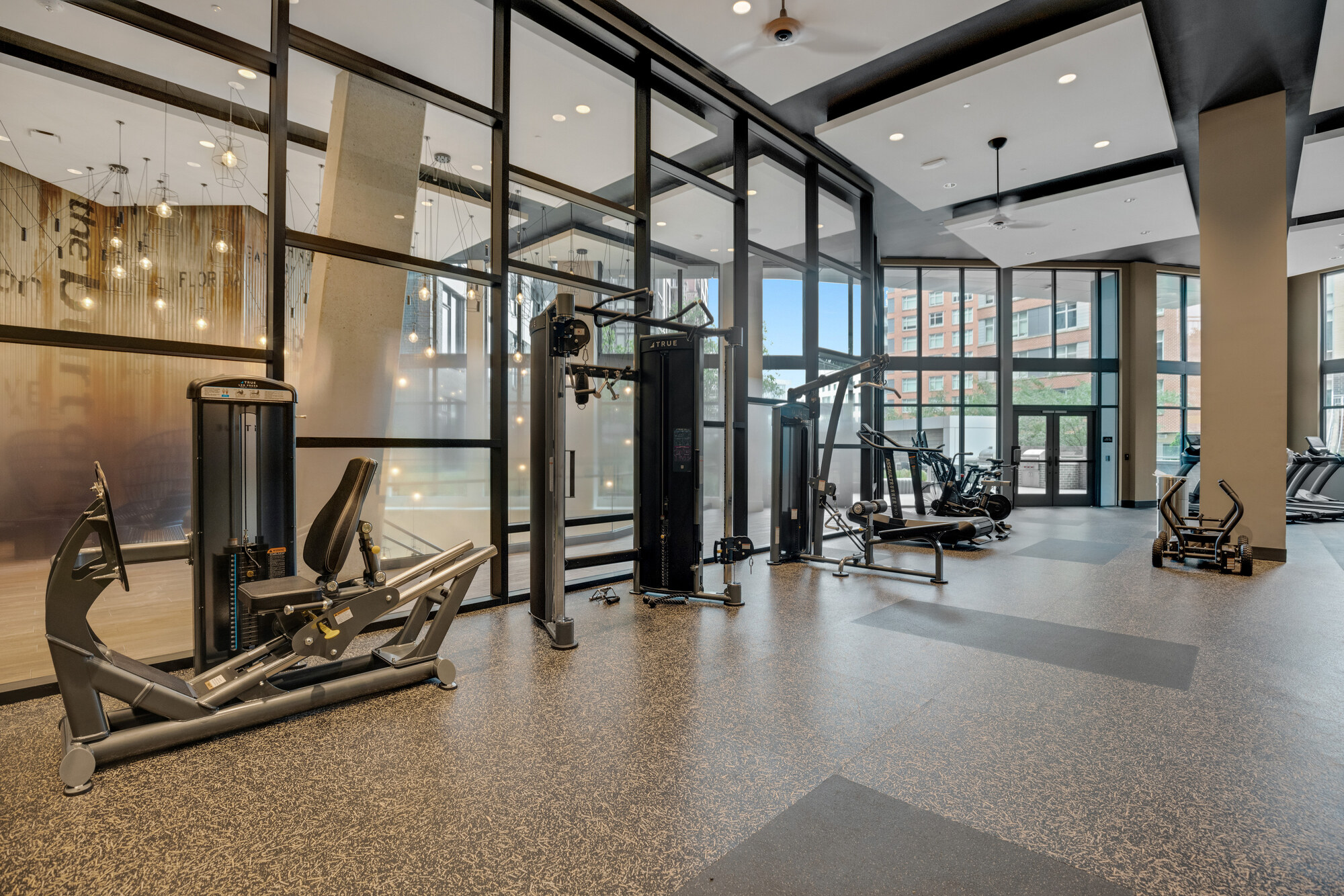 Upscale glass-walled fitness centre with strength machines and a lit lobby beyond