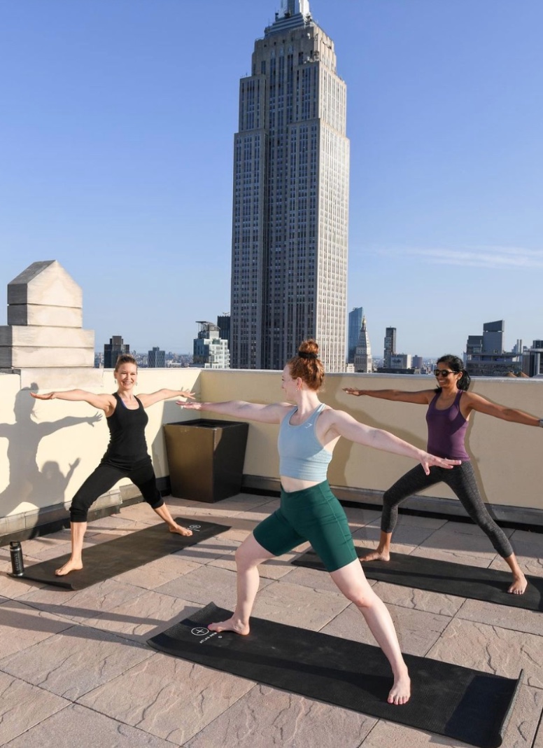 Three people in a rooftop yoga class with the Empire State Building behind them