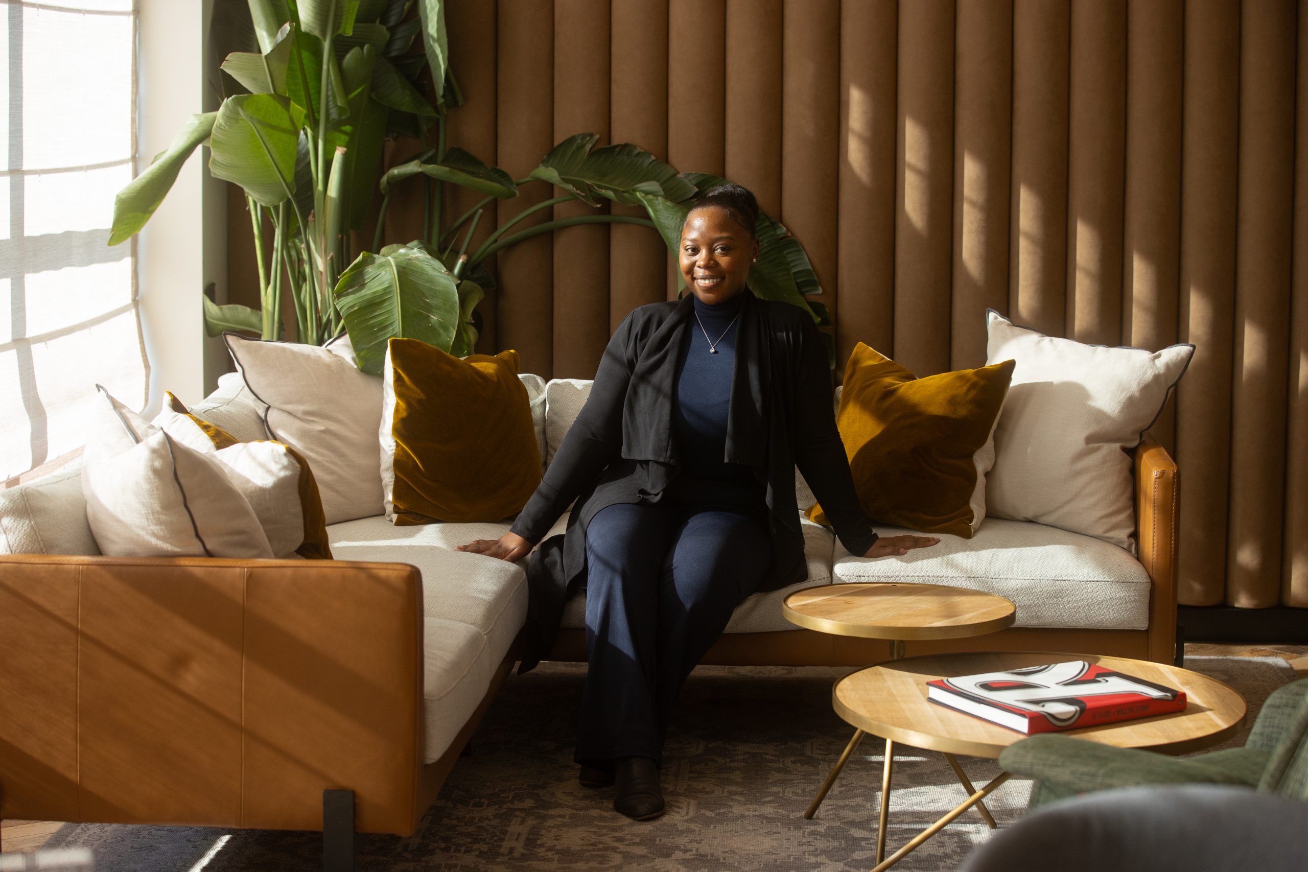 Team member seated on a sofa in a sunlit residential lounge with plants and soft furnishings