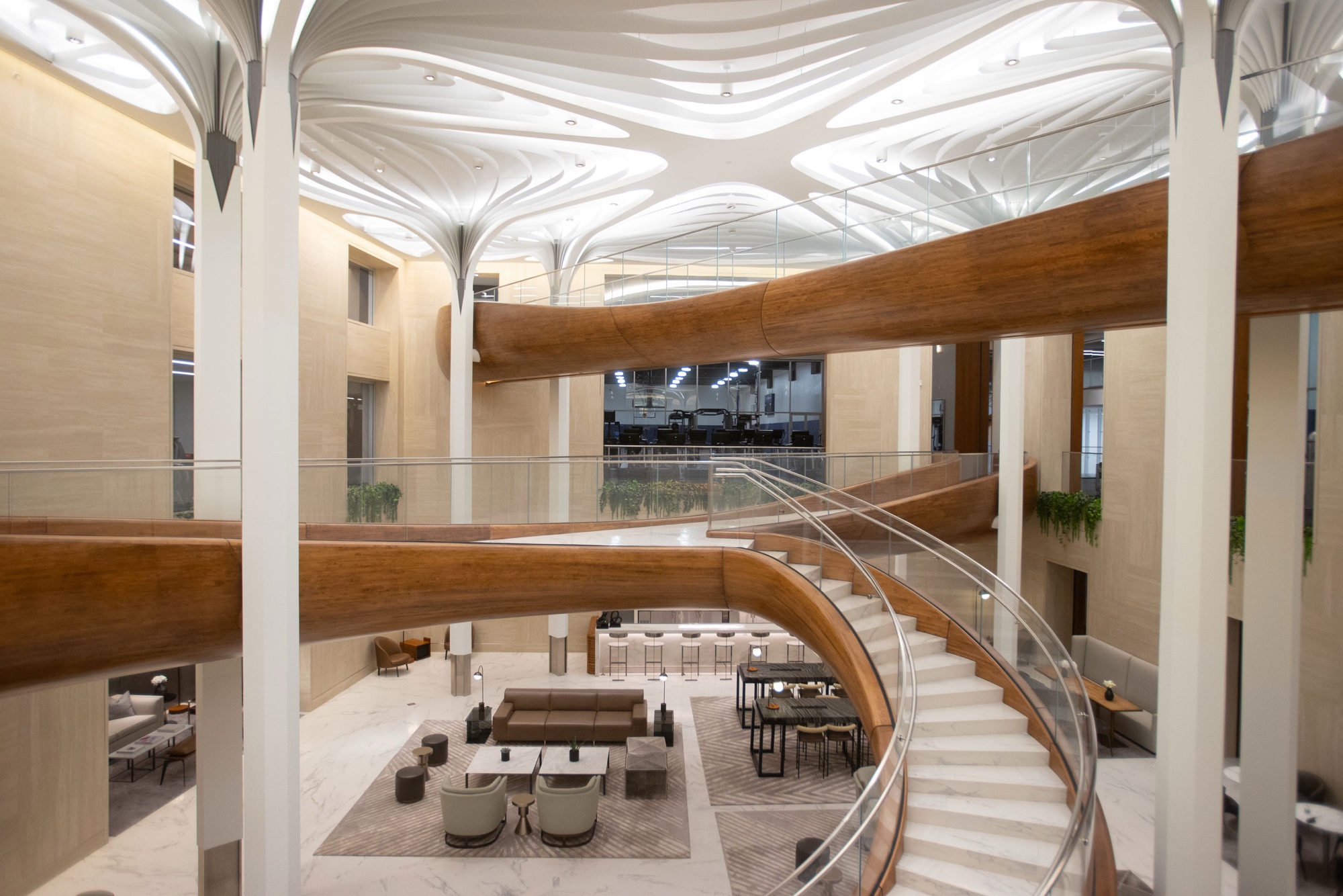 Light-filled atrium lobby with a curved staircase, sculptural ceiling canopy and lounge seating