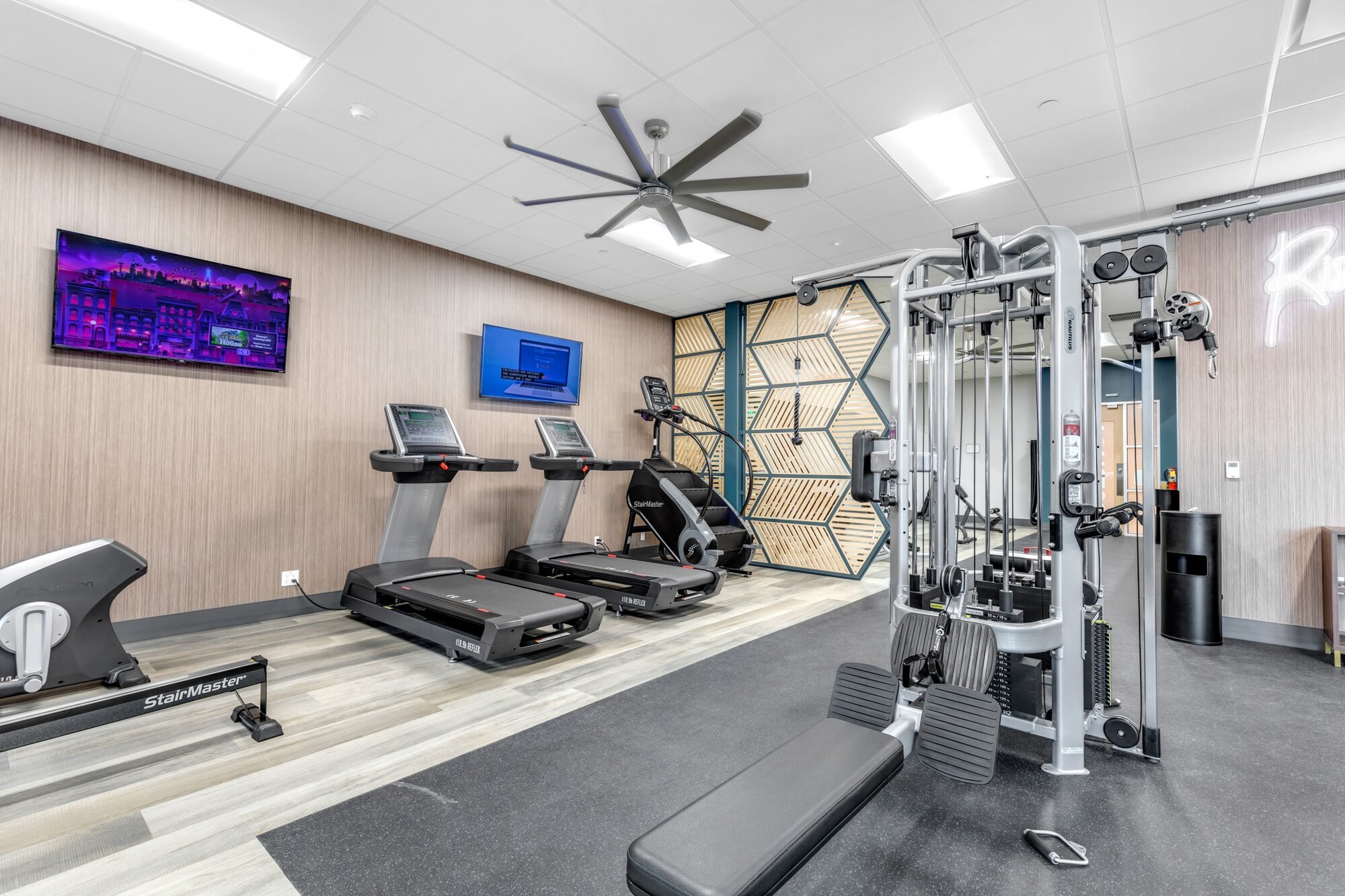 Compact amenity gym with treadmills, a cable machine and a wood-panelled feature wall