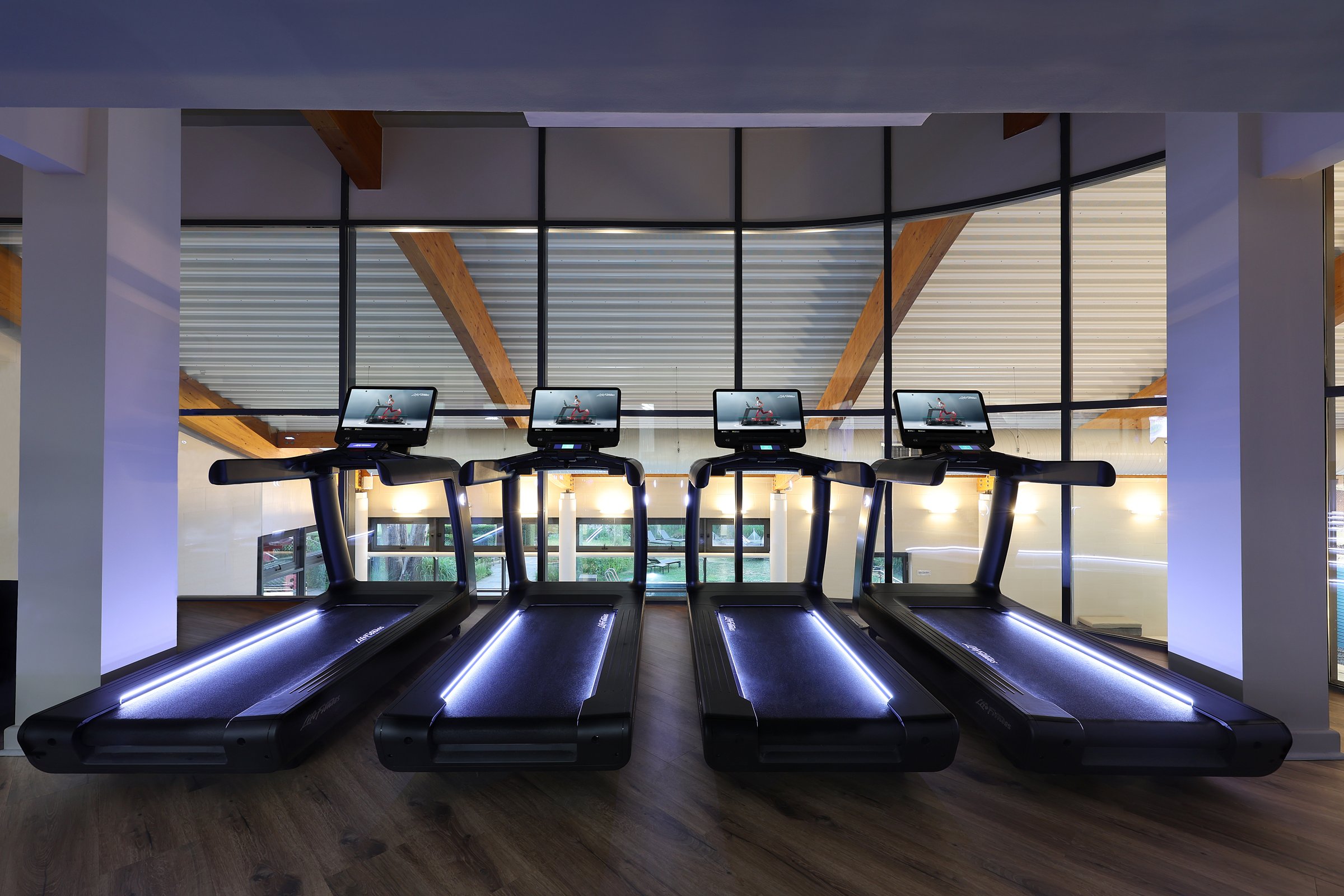 Row of treadmills under a curved wood ceiling with glass walls