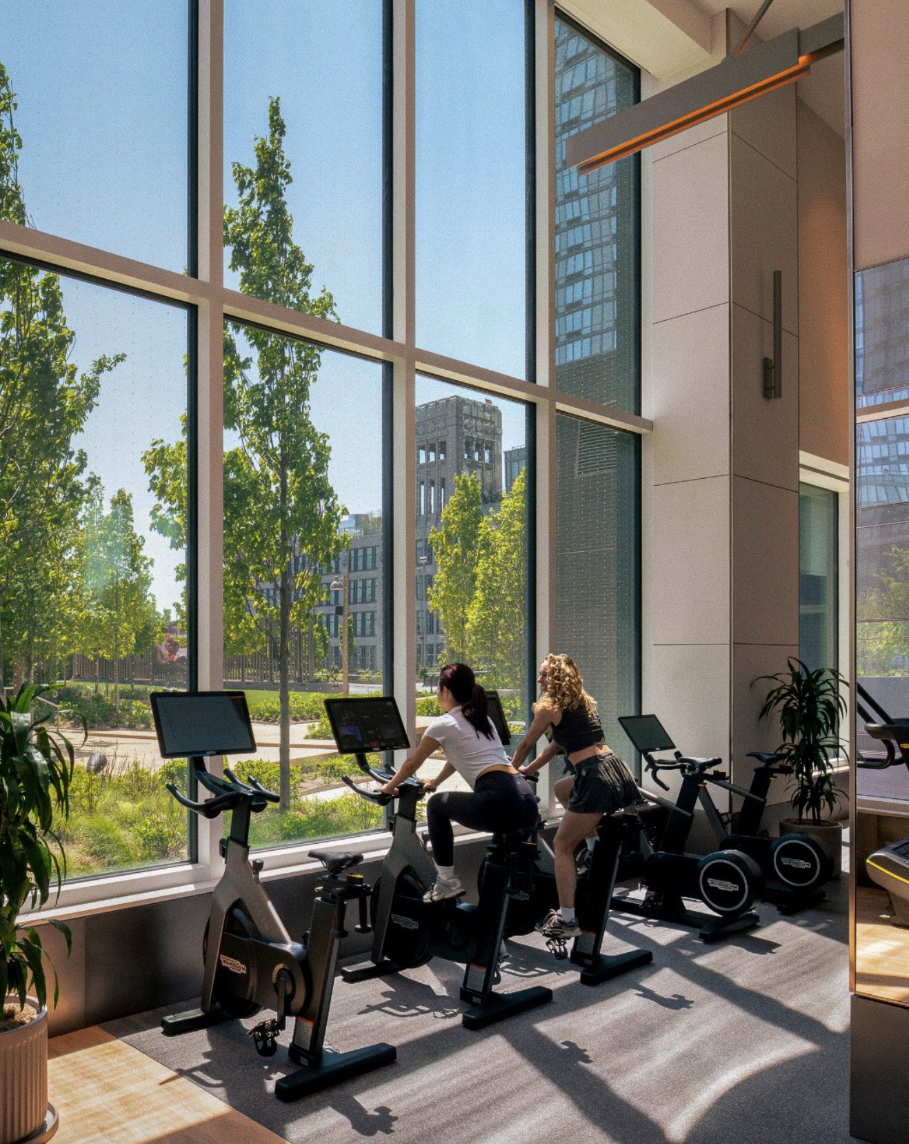 Member riding a stationary bike beside floor-to-ceiling windows