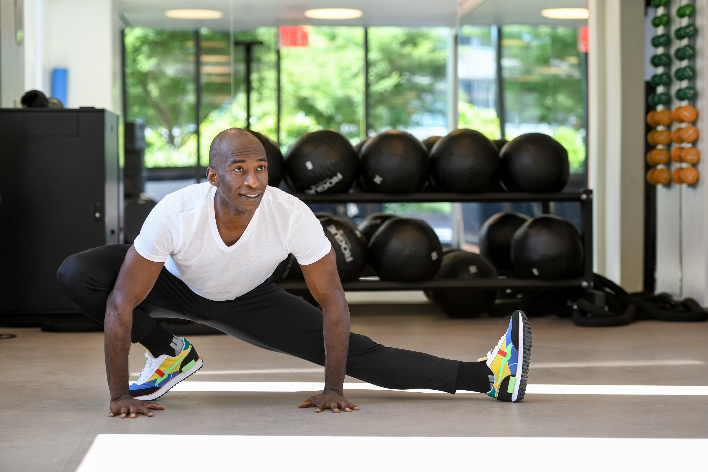 Man stretching in a side lunge in front of a rack of medicine balls