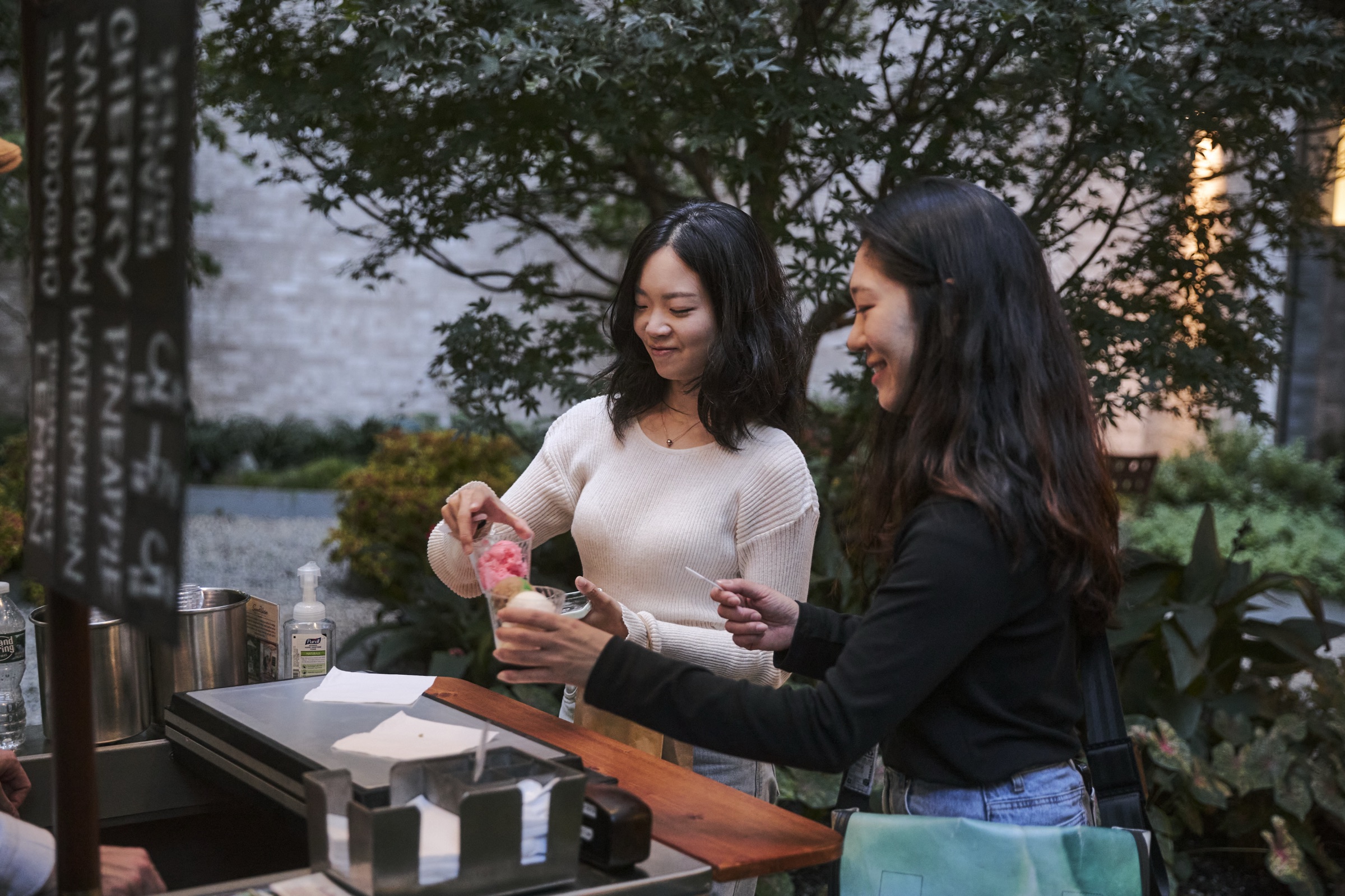 Two women pouring smoothies at an outdoor juice bar