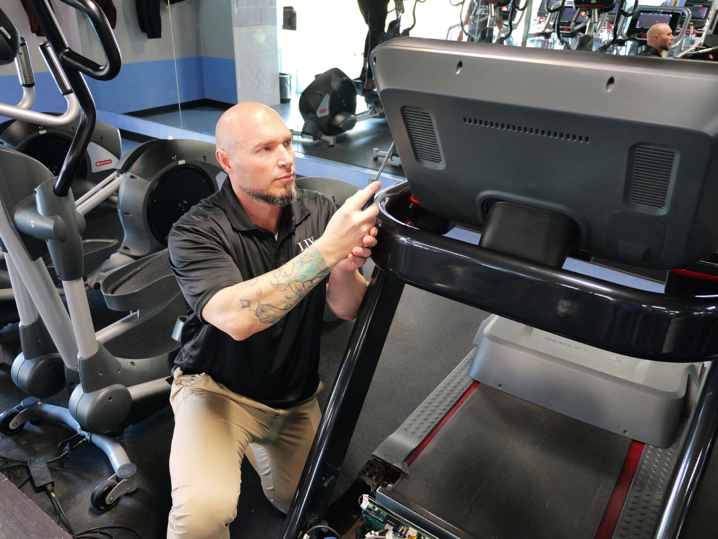 Technician servicing a treadmill console in a fitness center