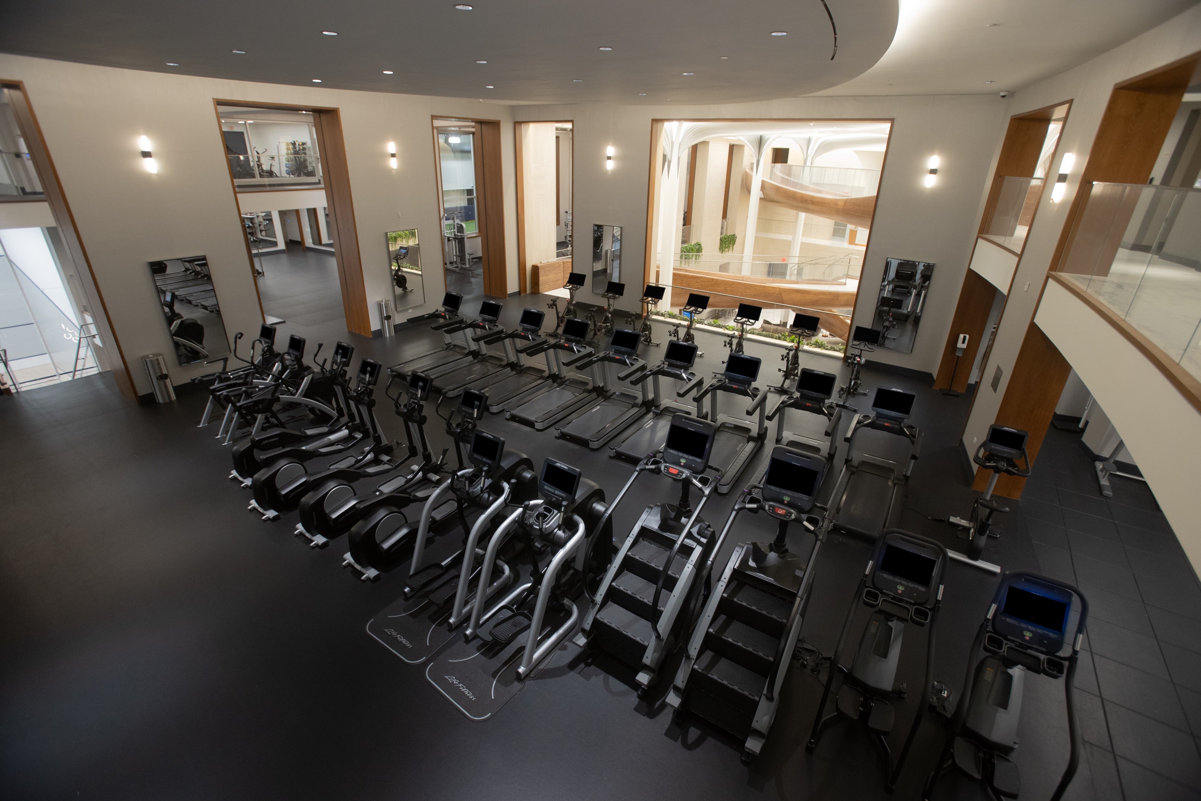 Rows of cardio equipment in a bright fitness center with skylights