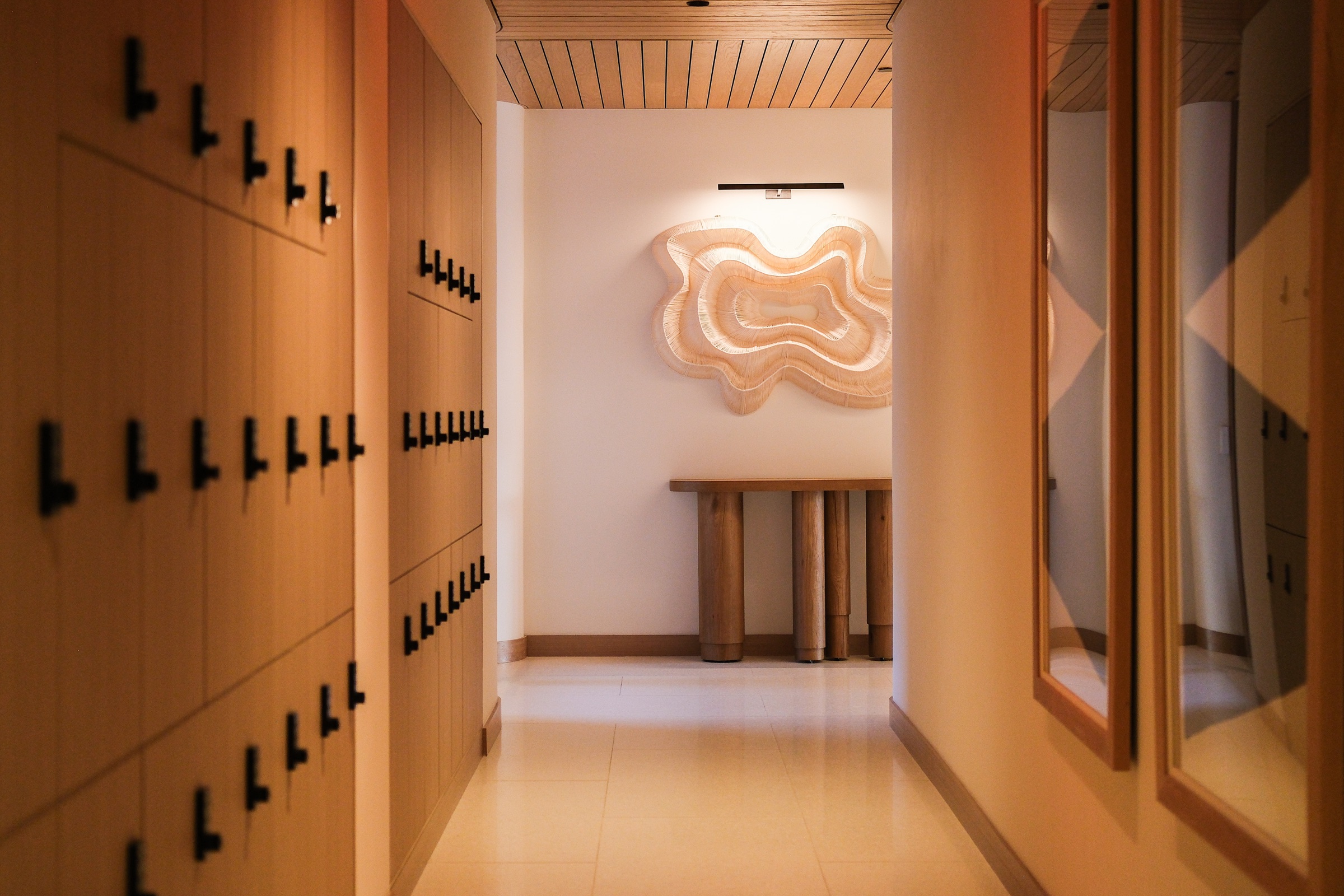 Wood-clad locker corridor with a sculptural wall feature