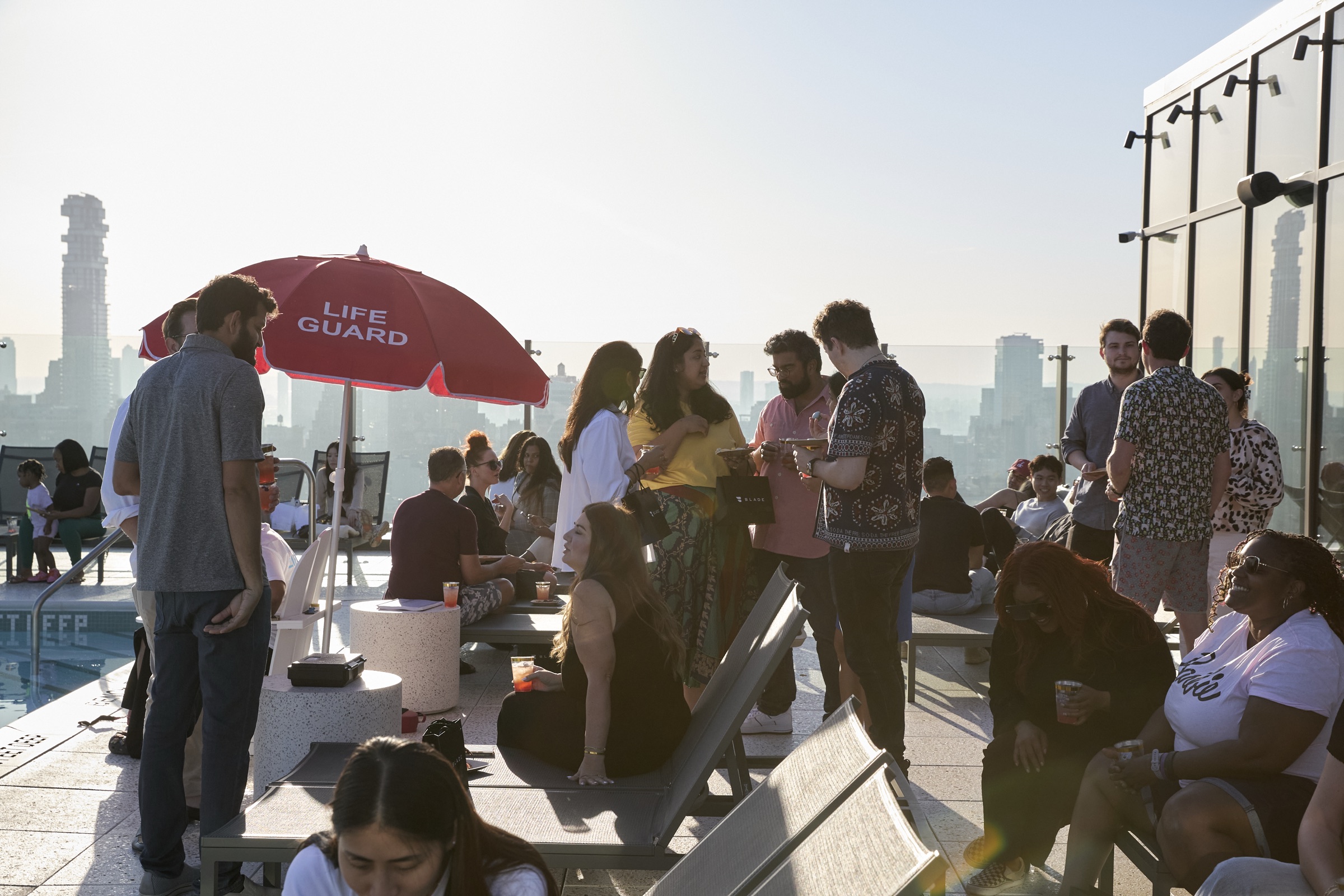 Residents mingling at a rooftop social event beside a lifeguard umbrella
