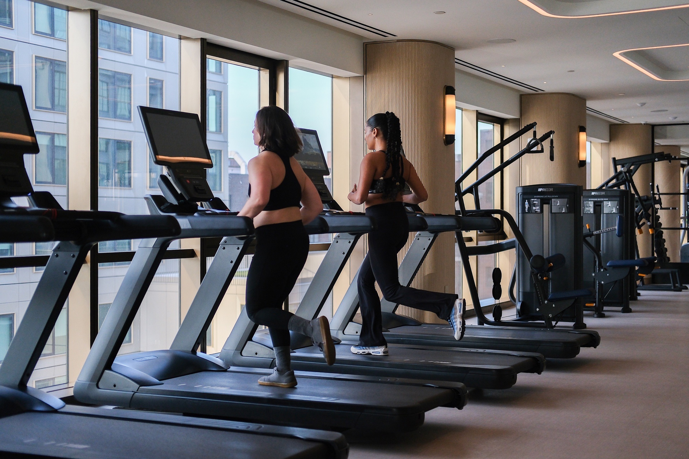 Two women running on treadmills in a high-rise fitness center